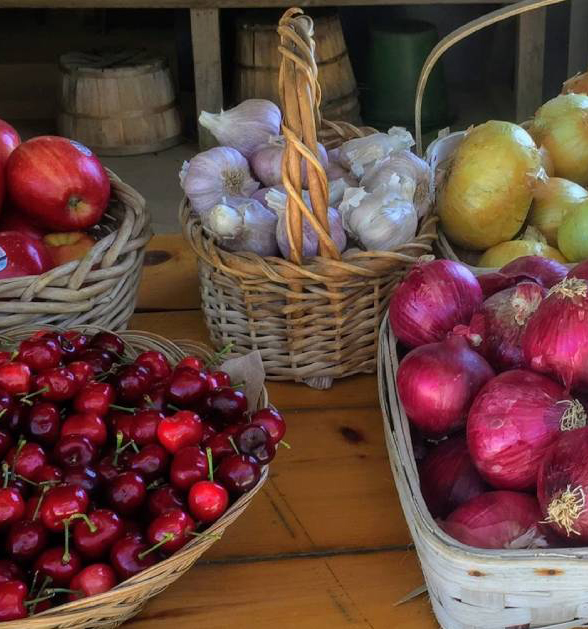 Close up of cherries, apples, red onions, white onions, and garlic in baskets.