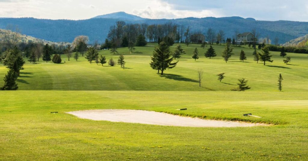 Another golf course view with beautiful green grass and mountains in the background.