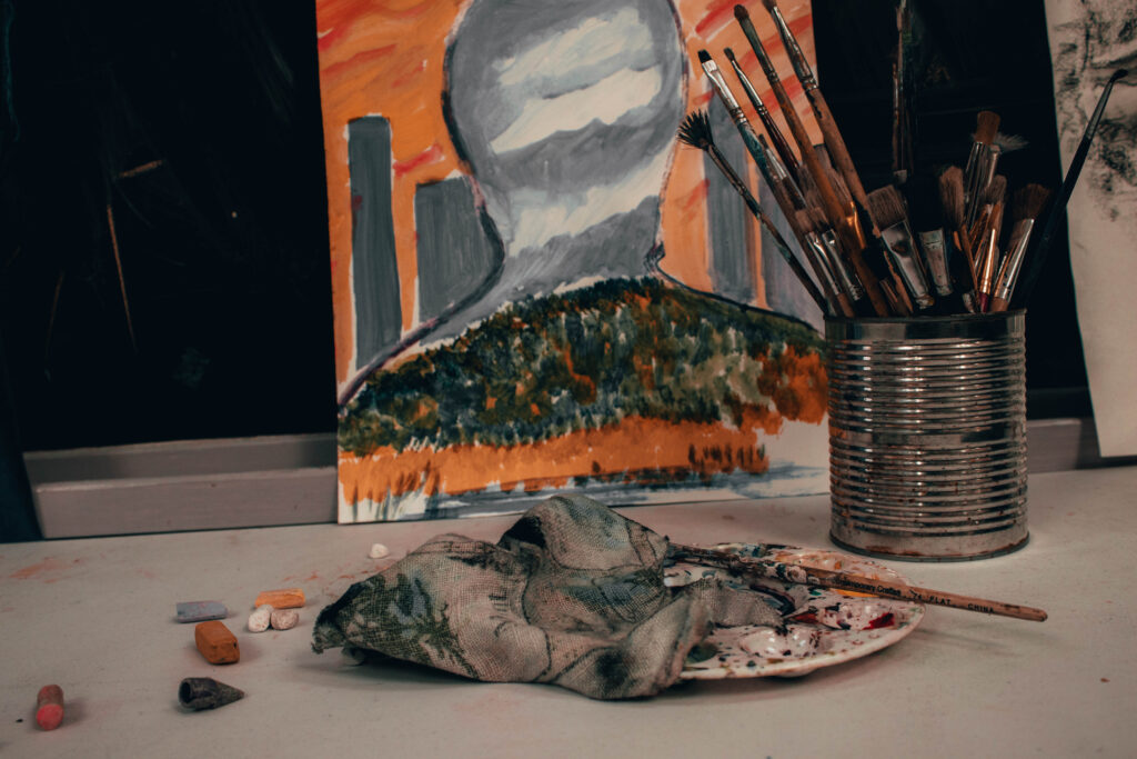 A metal can holding brushes and a painting is seen behind it