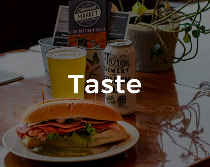 A table containing a sandwich and beer with the restaurant menu shown in the background along with a small plant and the word Tasted overlaid on it.